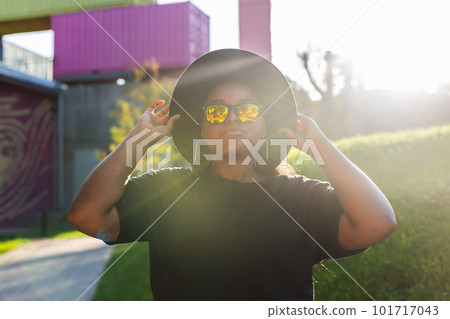 Happy African american young woman wearing t-shirt laughing looking at camera standing on street. Smiling generation z hipster girl posing outdoor backlit with sunlight portrait Happy African american young woman wearing t-shirt laughing looking at camera standing on street. Smiling generation z hipster girl posing outdoor backlit with sunlight portrait 101717043