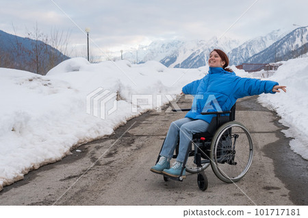 A woman in a wheelchair spread her arms to the side like wings in the mountains in winter. A woman in a wheelchair spread her arms to the side like wings in the mountains in winter. 101717181