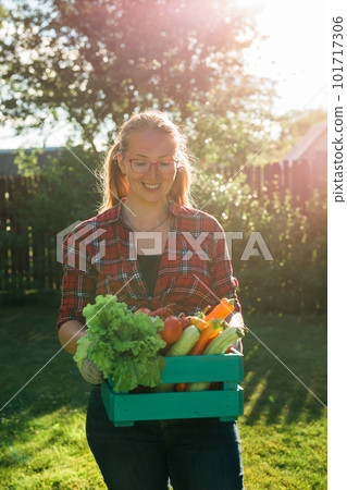 Female farmer carrying box of picked vegetables - garden and harvesting agricultural product for online selling. 101717306
