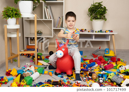 A little boy is jumping on an inflatable rubber donkey among the mess in the children's room. Bouncing toy for kids. 101717499