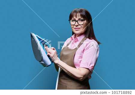 Woman in apron posing with iron, on blue background 101718892
