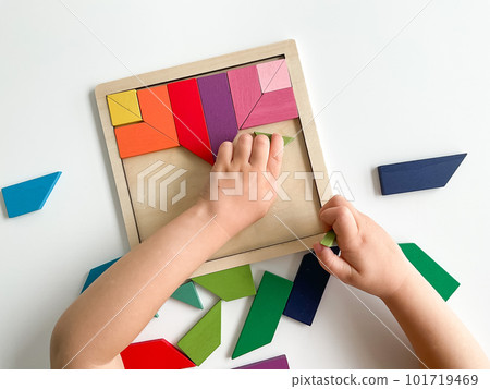 childs hand collects multicolored wooden mosaic on white background. 101719469