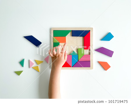 childs hand collects multicolored wooden mosaic on white background. 101719475