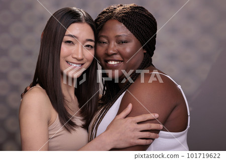 Two diverse women hugging demonstrating confidence, love and self care. Beautiful african american and asian young girlfriends smiling, embracing together and looking at camera Two diverse women hugging demonstrating confidence, love and self care. Beautiful african american and asian young girlfriends smiling, embracing together and looking at camera 101719622