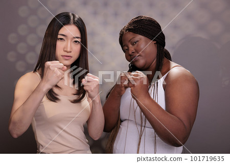 African american and asian women standing in fighter pose, demonstrating girls power. Strong diverse models with different body shapes and ethnicity fighting and showing fists African american and asian women standing in fighter pose, demonstrating girls power. Strong diverse models with different body shapes and ethnicity fighting and showing fists 101719635