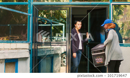 African american courier delivering pizza box order at front door, working at restaurant food delivery. Deliveryman giving pizzeria meal package to female client, takeaway express service. 101719647