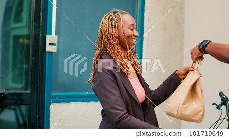 African american worker delivering takeaway order to client, giving paperbag with lunch meal at office entrance. Food delivery courier holding restaurant fastfood package. Handheld shot. 101719649