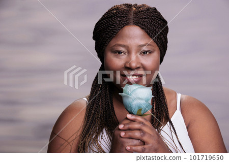Body positive african american woman posing with blue rose, holding feminine symbol in hands and looking at camera. Smiling woman with healthy skin and flower in arms portrait Body positive african american woman posing with blue rose, holding feminine symbol in hands and looking at camera. Smiling woman with healthy skin and flower in arms portrait 101719650
