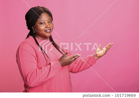 Portrait of attractive young adult advertising promotional product in studio, posing for advertisement over pink background. Confident woman with stylish hairstyle looking at camera during ad shoot Portrait of attractive young adult advertising promotional product in studio, posing for advertisement over pink background. Confident woman with stylish hairstyle looking at camera during ad shoot 101719669