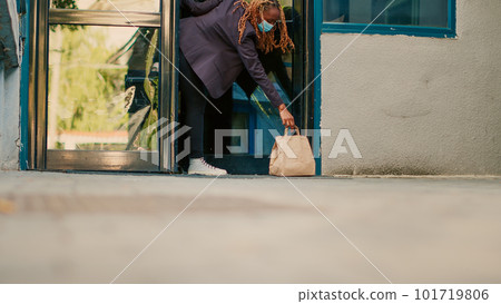 Female carrier letting fastfood order package at front door, client picking up paperbag with restaurant lunch. Takeaway service courier delivering food during covid 19 pandemic, wearing facemask. Female carrier letting fastfood order package at front door, client picking up paperbag with restaurant lunch. Takeaway service courier delivering food during covid 19 pandemic, wearing facemask. 101719806
