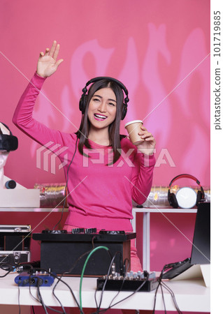 Happy performer playing techno sound at professional mixer console while drinking coffee, enjoying playing songs at night in club. Asian musician creating musical performance with remix music Happy performer playing techno sound at professional mixer console while drinking coffee, enjoying playing songs at night in club. Asian musician creating musical performance with remix music 101719885