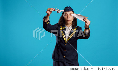 Positive stewardess playing with toy and paper plane, having fun with origami and mini artificial airplane in studio. Happy air hostess wearing flying uniform working in aviation industry. 101719940