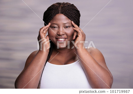 African american woman doing face massage skincare routine, touching face with fingers and looking at camera. Plus size smiling beauty model putting hands on fresh clean skin portrait African american woman doing face massage skincare routine, touching face with fingers and looking at camera. Plus size smiling beauty model putting hands on fresh clean skin portrait 101719987