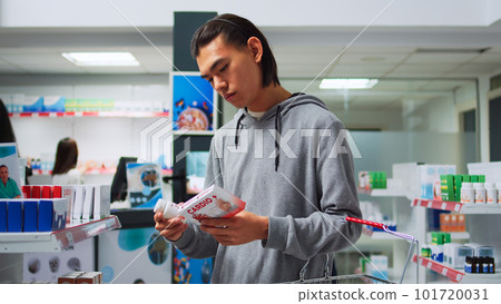 Male customer looking at cardiology drugs to buy from drugstore, trying to cure heart problems. Young man reading packages of pills and vitamins, carrying basket with pharmaceutical products. Male customer looking at cardiology drugs to buy from drugstore, trying to cure heart problems. Young man reading packages of pills and vitamins, carrying basket with pharmaceutical products. 101720031