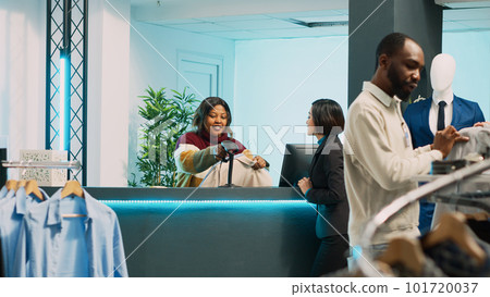 Asian person buying fashion collection in boutique shop, making electronic payment at pos terminal. Young client talking to store employee at cash register before transaction, small business. Asian person buying fashion collection in boutique shop, making electronic payment at pos terminal. Young client talking to store employee at cash register before transaction, small business. 101720037