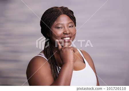 African american smiling beauty plus size model pointing on clean skin, holding finger on cheek and looking at camera. Attractive woman posing in studio with positive facial expression African american smiling beauty plus size model pointing on clean skin, holding finger on cheek and looking at camera. Attractive woman posing in studio with positive facial expression 101720110