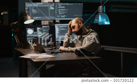 Young man feeling tired and working on programming code, typing database information and html script on laptop. Adult falling asleep at office, being exhausted using terminal window. Handheld shot. 101720122