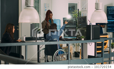 Asian programer with chronic impairment working on software code with it engineer in agency office. App developer with disability in wheelchair using html script on temrinal window. Asian programer with chronic impairment working on software code with it engineer in agency office. App developer with disability in wheelchair using html script on temrinal window. 101720154