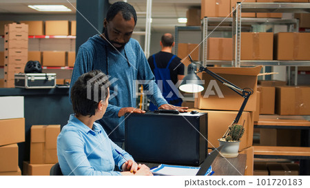 Small business owners using laptop to do shipment logistics work, preparing merchandise order from storage room racks. Young people working on startup retail development, supply chain. Small business owners using laptop to do shipment logistics work, preparing merchandise order from storage room racks. Young people working on startup retail development, supply chain. 101720183