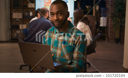 African american office employee working on laptop portrait, front view. Smiling man holding computer, looking at camera medium shot, company financial presentation, business meeting African american office employee working on laptop portrait, front view. Smiling man holding computer, looking at camera medium shot, company financial presentation, business meeting 101720184