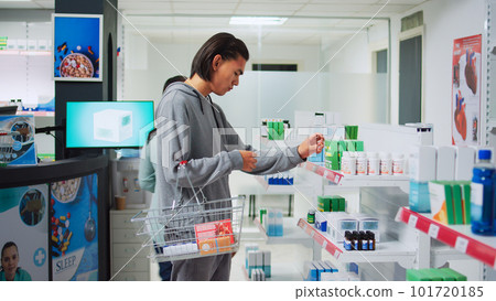 Male customer analyzing supplements boxes on pharmacy shelves, examining vitamins to buy prescription treatment. Checking medical products and drugs at healthcare drugstore shop. 101720185