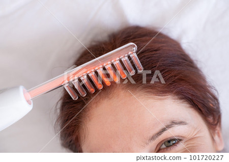 Caucasian woman on a hair care procedure using the Darsonval apparatus. 101720227