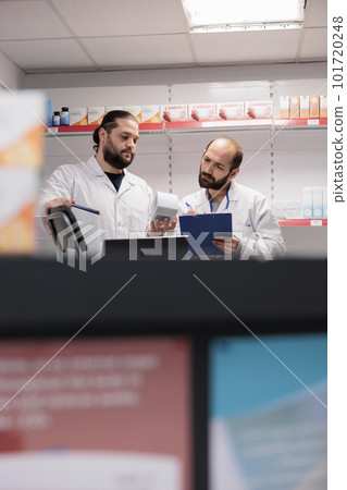 Caucasian colleagues standing at drugstore counter desk doing medication and pharmaceutical products inventory in pharmacy. Workers is trained to recognize and address any potential drug interactions Caucasian colleagues standing at drugstore counter desk doing medication and pharmaceutical products inventory in pharmacy. Workers is trained to recognize and address any potential drug interactions 101720248