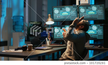 Programming thief celebrating hacking success in office late at night, working with multiple monitors to steal password. Cheerful hacker with hidden identity feeling pleased about achievement. 101720281