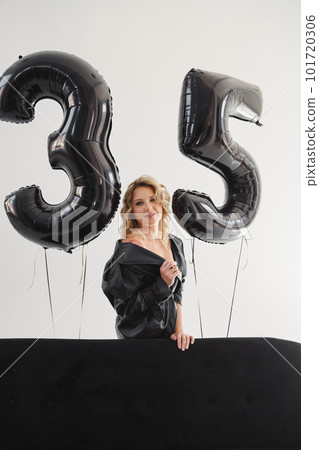 a naked blonde with tattoos in a black coat by a black sofa. birthday 101720306