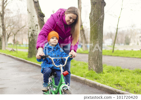 Young mom teaching son to ride bike first time in park Young mom teaching son to ride bike first time in park 101720420