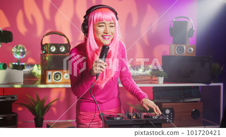 Musician having fun performing techno music at party in nightclub, using professional audio equipment. Asian performer with pink hair mixing electronic sound using mixer console. Dj concept Musician having fun performing techno music at party in nightclub, using professional audio equipment. Asian performer with pink hair mixing electronic sound using mixer console. Dj concept 101720421
