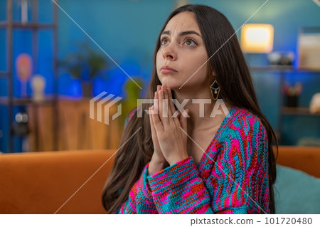 Young woman girl praying sincerely with folded arms asking God for help begging apology on home sofa 101720480