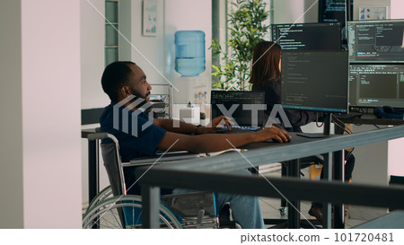 Software developer wheelchair user working on html script code, checking database and server to develop app system. Coder with chronic impairment using programming source in it office. 101720481