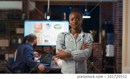 Smiling african american businesswoman crossing arms portrait, front view medium shot. Company employee standing in boardroom doorway in coworking space, coworkers presentation in background 101720552