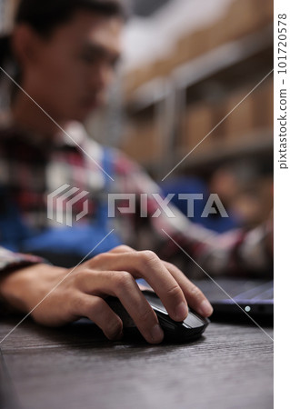 Warehouse worker creating parcel invoice on laptop in storage room. Storehouse employee sitting at desk, analyzing freight logistics report while using computer mouse close up 101720578