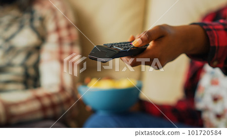 Woman switching channels with tv remote control to watch movie with her partner, eating chips and drinking beer at home. Modern people looking for show. Close up. Handheld shot. 101720584