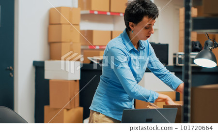 Young adult using merchandise from warehouse to prepare order, shipping products before doing inventory. Female employee planning distribution management, woking on business development. 101720664