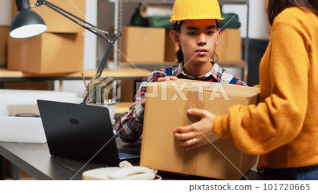 Young person doing warehouse inventory with pc, organizing products in packages on racks. Male employee working in storage room to plan order shipment, merchandise distribution. 101720665