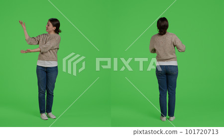 Friendly person doing advertisement and example sign in studio, standing over full body green screen backdrop. Casual relaxed woman showing presentation icon and advertising something. 101720713