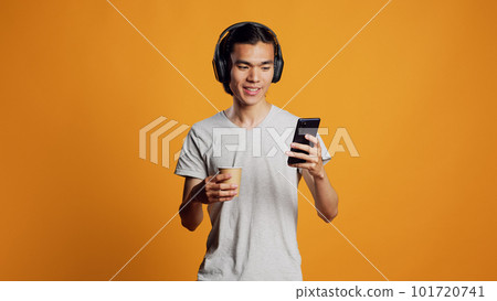 Modern person listening to music and using smartphone, having fun with mp3 songs on headphones. Young asian man enjoying sound with audio headset, checking smartphone app on camera. 101720741