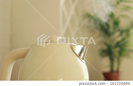 Close up of boiling water and steam comes out of white modern electric kettle. Teapot for hot drinks against background of houseplant in kitchen. Concept of coffee or tea break. Healthy lifestyle Close up of boiling water and steam comes out of white modern electric kettle. Teapot for hot drinks against background of houseplant in kitchen. Concept of coffee or tea break. Healthy lifestyle 101720894