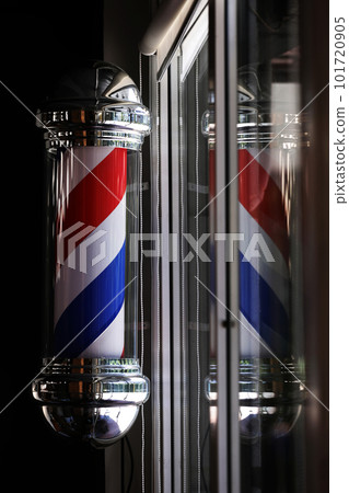 Barber pole spinning at night. International barbershop pole sign. A barber pole calling for people at street. Vintage barbershop. Salon. 101720905