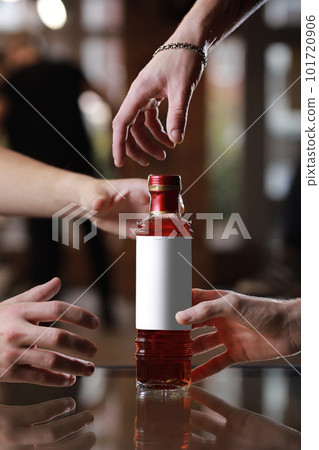 Glass bottle with alcohol drink with mockup on mirror table. Male people's hands reach for the bottle. Concept of celebration holiday in pub Glass bottle with alcohol drink with mockup on mirror table. Male people's hands reach for the bottle. Concept of celebration holiday in pub 101720906