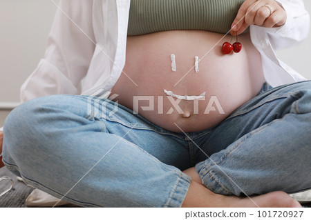 Close-up of torso of young pregnant model applying moisturizer on her belly to avoid stretch marks. Future mom with funny smile from moisturizing cream on her tummy. Pregnancy skincare concept 101720927