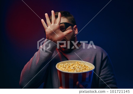 A man is in a dark room with neon lighting, watching a movie with 3D glasses and popcorn. A man is in a dark room with neon lighting, watching a movie with 3D glasses and popcorn. 101721145