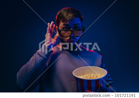 A man is in a dark room with neon lighting, watching a movie with 3D glasses and popcorn. A man is in a dark room with neon lighting, watching a movie with 3D glasses and popcorn. 101721191