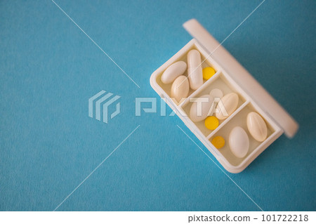 different capsules lie in a white open pill box on a blue background. View from above 101722218