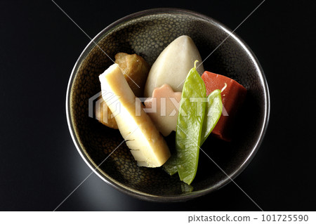 A bird's-eye view of a simmered dish containing bamboo shoots, taro, namafu, snow peas, etc. against a black background 101725590