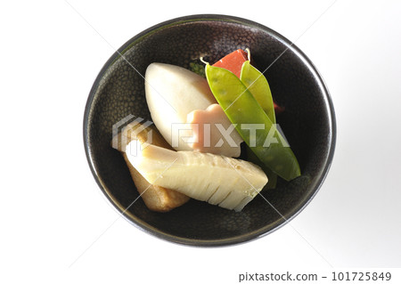 A bird's-eye view of a simmered dish containing bamboo shoots, taro, namafu, snow peas, etc. against a white background 101725849