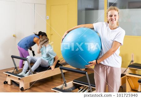 Portrait of girl standing with fitness ball during pilates training at gym Portrait of girl standing with fitness ball during pilates training at gym 101725940